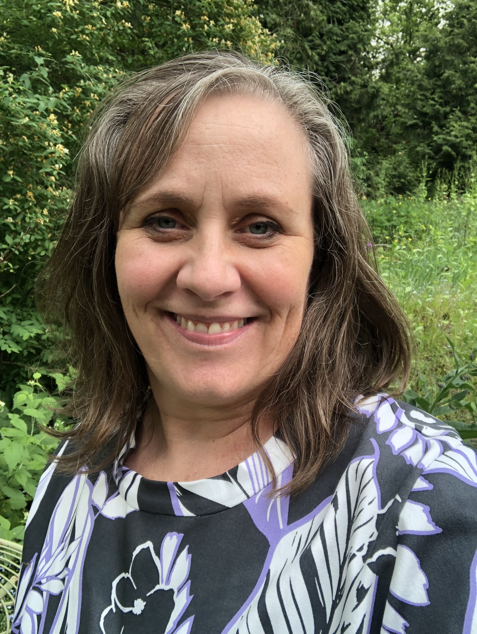 Photo of a blonde woman with long hair wearing a blue shirt in front of a brick wall