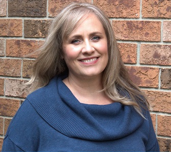 Photo of Shanan Cunnington - a blonde woman with long hair wearing a blue shirt in front of a brick wall
